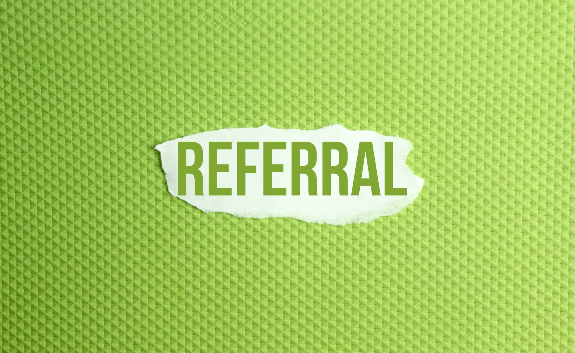 a torn paper written with inscription referral on a green background